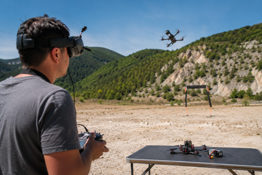 Навчання FPV-пілотуванню: з чого почати Пілот у FPV-окулярах керує гоночним дроном під час тренування на відкритому майданчику в гірській місцевості.